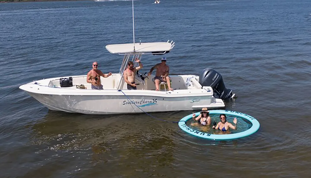 A group of people is enjoying a sunny day out on the water with some on a boat and others in an attached floating ring