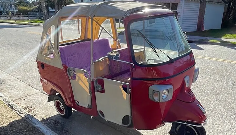 The image shows a quirky three-wheeled red vehicle with a clear flexible canopy enclosure and a plush purple interior