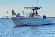 A group of people is enjoying a sunny day on a motorboat on calm waters with a bridge in the distant background.