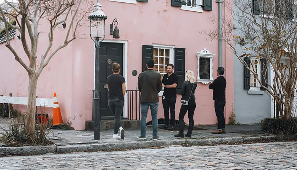 A group of people stands outside a pink building with a black door and windows possibly engaging in a conversation or waiting to enter