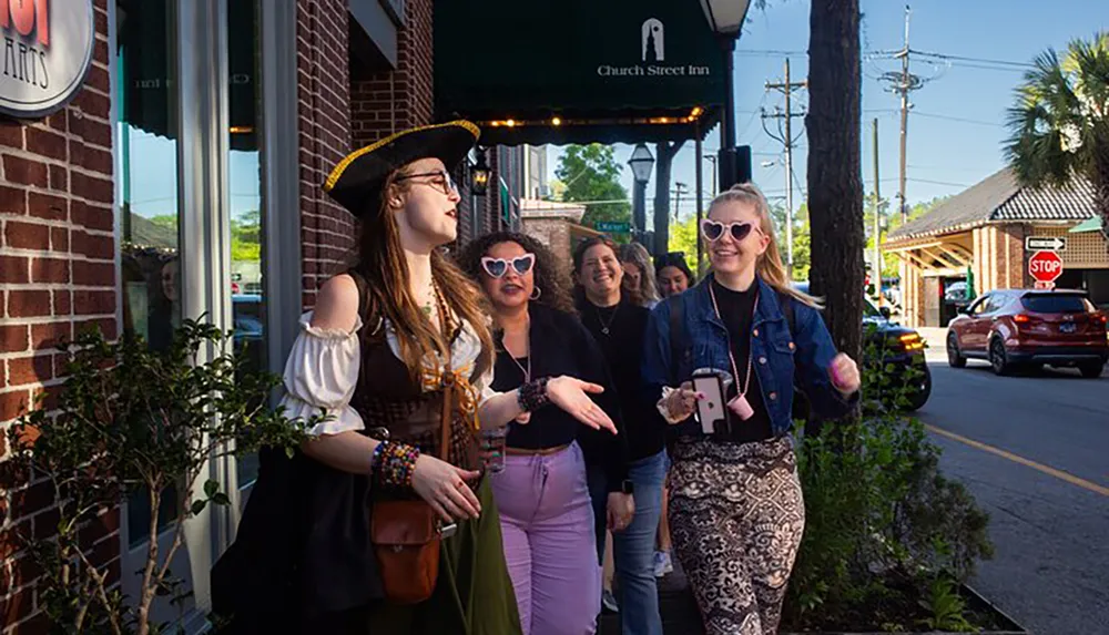 A group of people with one dressed in a pirate costume are walking and chatting happily on a sunny street by a building with a sign that reads Church Street Inn