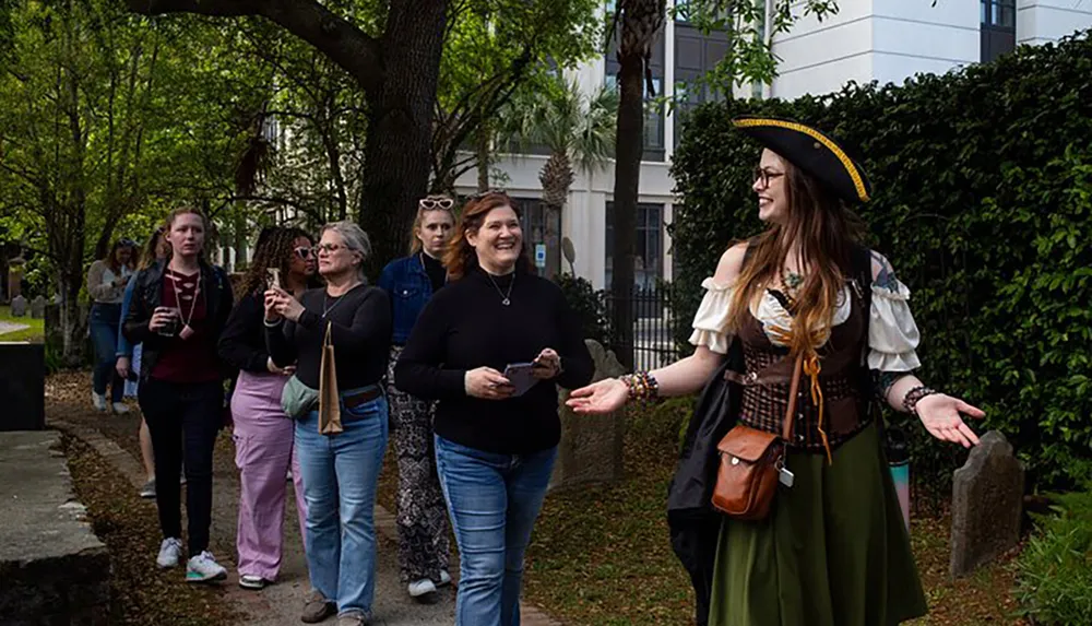 A person dressed in a pirate-inspired costume is enthusiastically guiding a group of attentive people through a historic-looking outdoor area