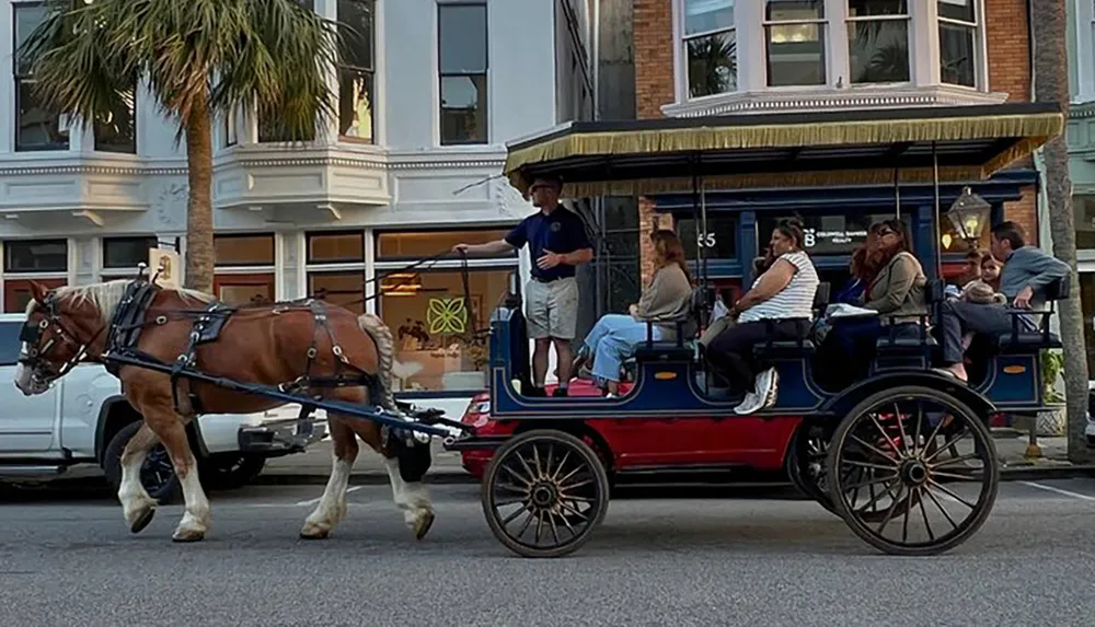 A horse-drawn carriage led by a single horse with a guide standing up front is carrying several passengers down a city street