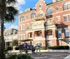 A horse-drawn carriage with passengers is moving along a street in front of a large traditional brick building with balconies possibly in a historic district