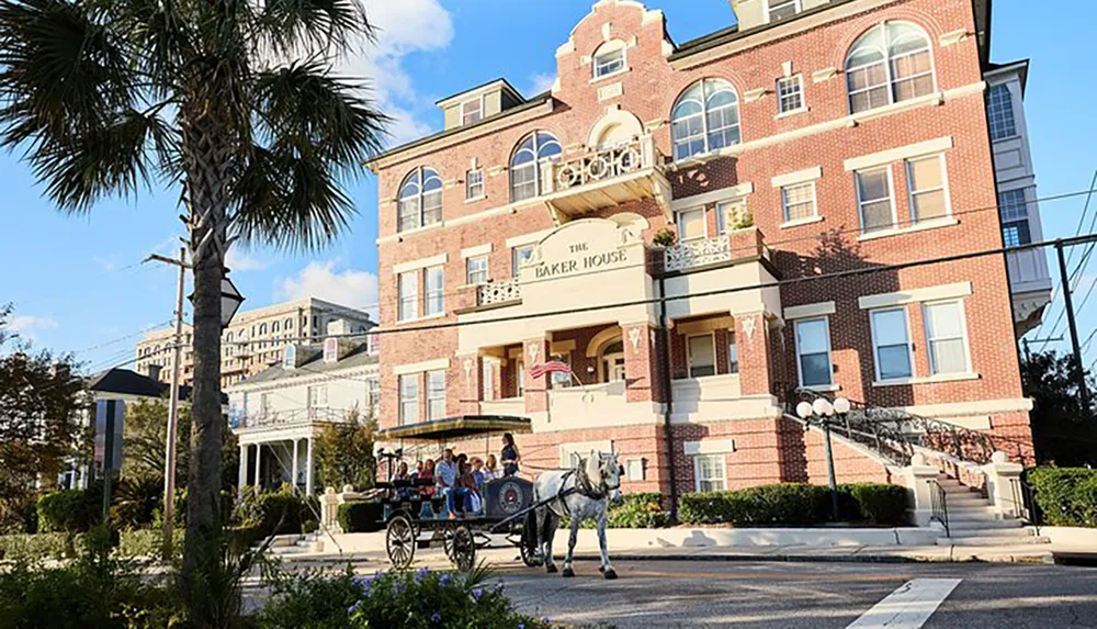 The image features a horse-drawn carriage with passengers in front of the Baker House a historic-looking brick building adorned with an American flag set against a backdrop of palm trees and a clear sky