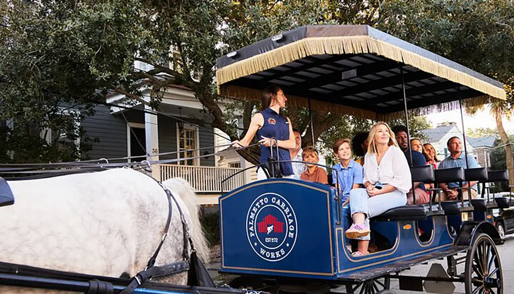 A group of people including children and adults enjoy a guided tour on a horse-drawn carriage through a leafy residential street