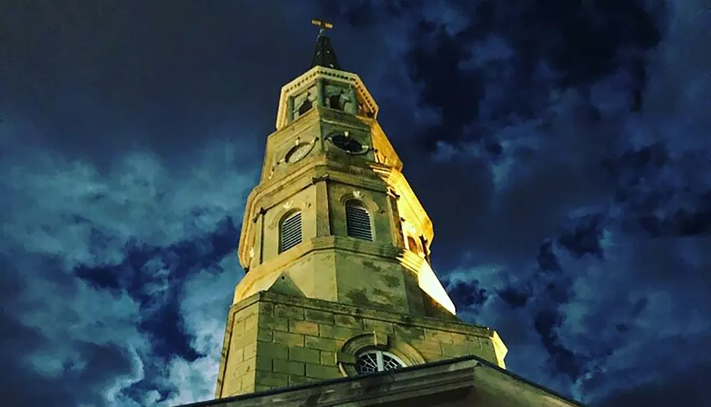 The image captures the illuminated steeple of a church against a dramatic evening sky filled with dark clouds