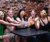 A group of five women wearing oversized heart-shaped sunglasses are enjoying drinks and smiling together at an outdoor table