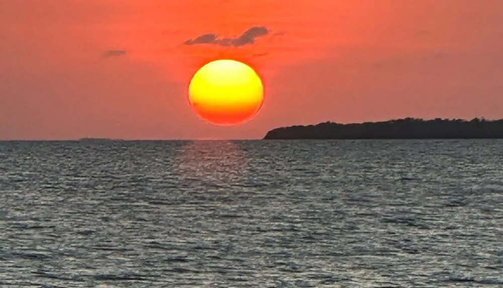 The image captures a vibrant sunset with a large glowing sun setting over the ocean casting a warm light on the water and painting the sky in shades of orange and red