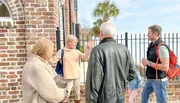 A group of people is engaged in conversation outside a brick building, likely on a guided tour or a casual outing.