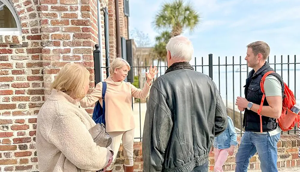 A group of people is engaged in conversation outside a brick building likely on a guided tour or a casual outing