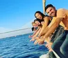 A group of smiling people are enjoying a sunny day on a sailboat with a city skyline and a large cruise ship in the background