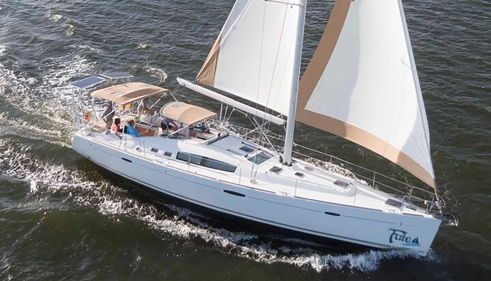 A group of people is enjoying a sunny day sailing on a large sailboat with its sails unfurled