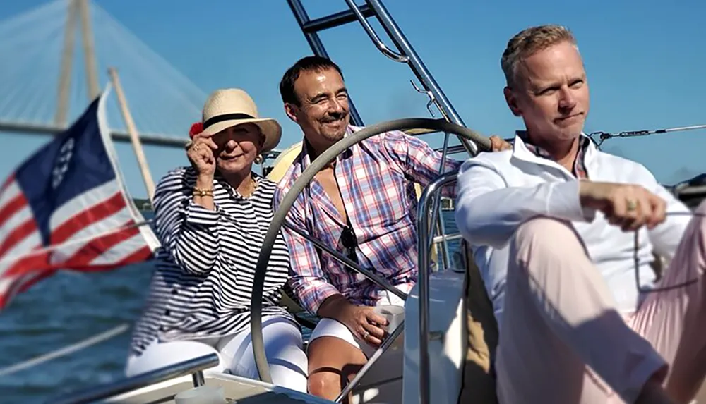 Three people are enjoying a sunny day on a sailboat with an American flag fluttering in the background