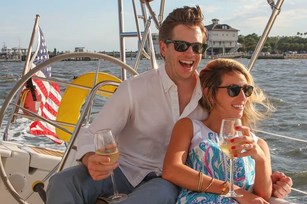 A happy couple is enjoying a sunny day on a sailboat each holding a glass of wine with the American flag in the background