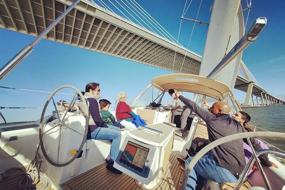 A group of people are enjoying a sunny day on a sailboat as they pass under a large bridge