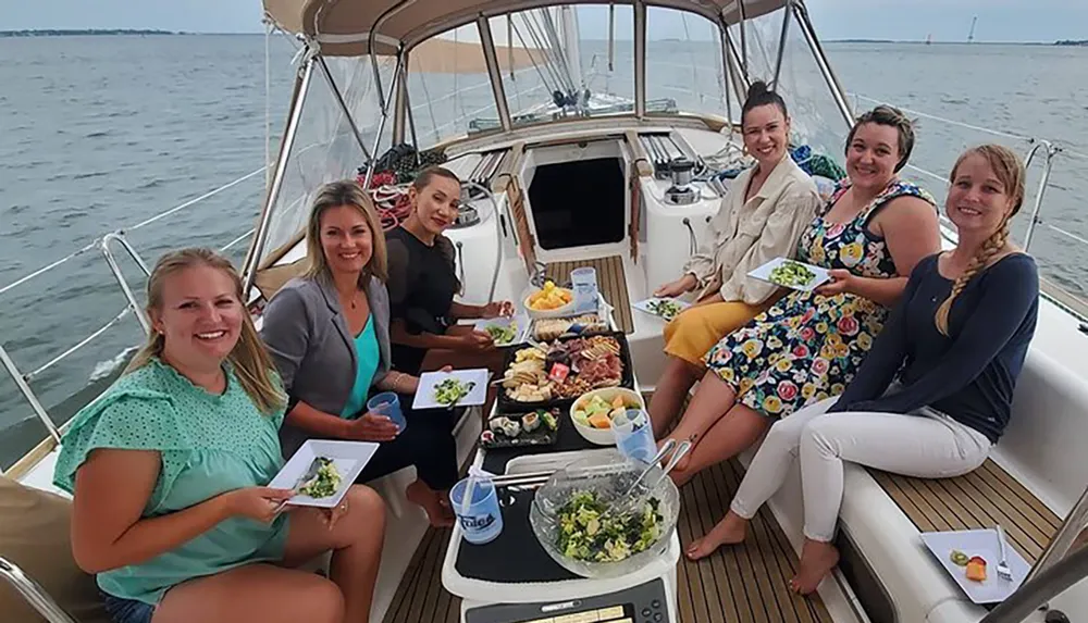 A group of smiling people are enjoying a meal together on a sailboat