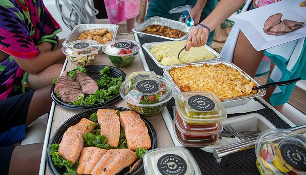 A variety of prepared dishes are spread out on a table as people serve themselves featuring items like grilled salmon sliced beef salads and casseroles