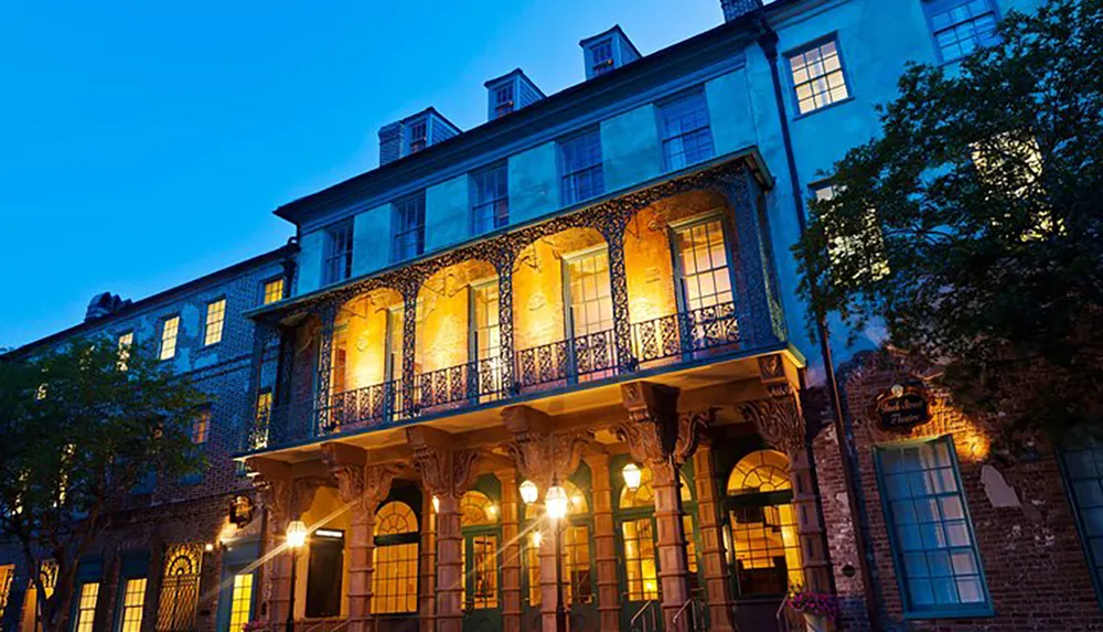 An elegant colonial building with a wrought-iron balcony is illuminated at dusk creating a warm and inviting atmosphere