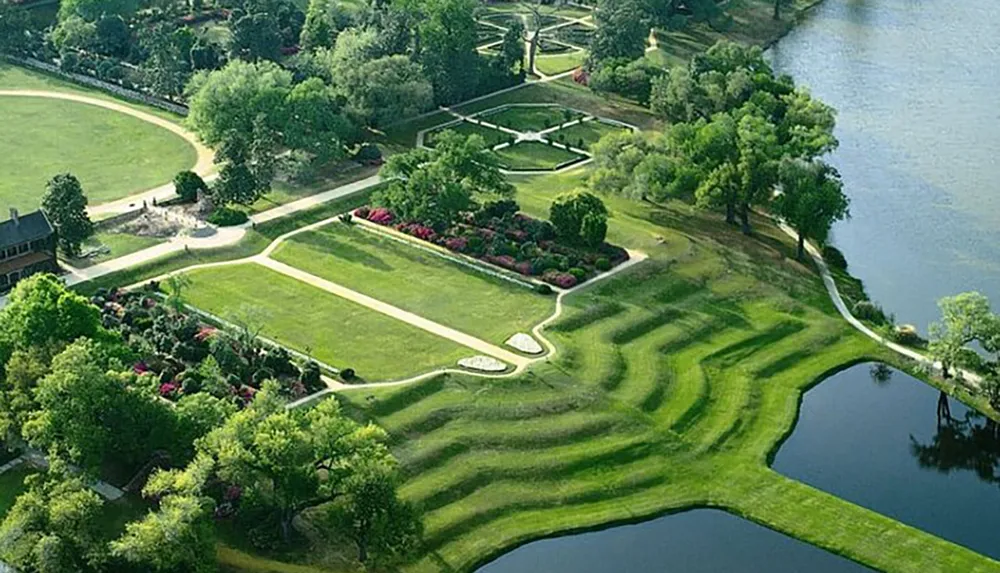 An aerial view of a meticulously landscaped park with geometric grass patterns and a body of water