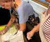 Three smiling people likely a family are wearing aprons and tasting food in a kitchen setting