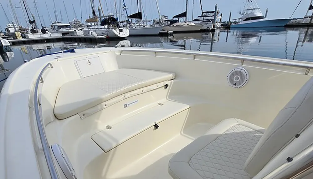 The image shows the interior seating area of a modern boat with cushioned benches set against the background of a peaceful marina filled with various yachts