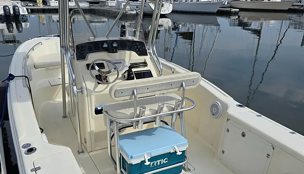 A center-console boat is docked at a calm marina with a cooler positioned in front of the helm