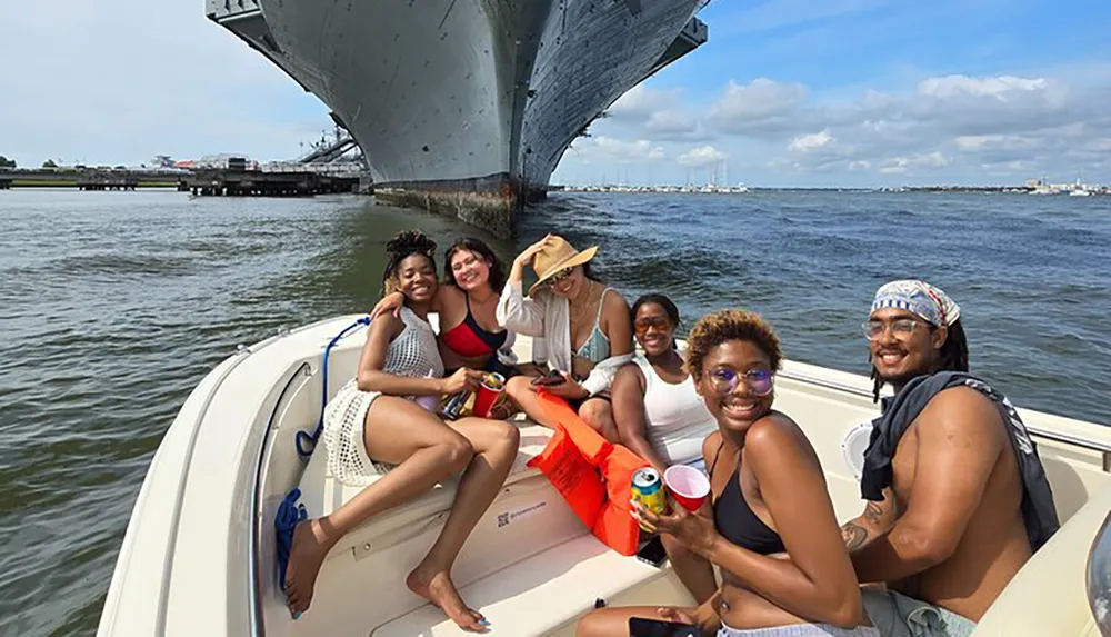 A group of friends is smiling and enjoying a sunny day on a boat with a large ship in the background