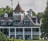 An elegant two-story house with a conical roof feature is nestled among large trees draped with Spanish moss overlooking a well-manicured lawn