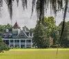 An elegant two-story house with a conical roof feature is nestled among large trees draped with Spanish moss overlooking a well-manicured lawn