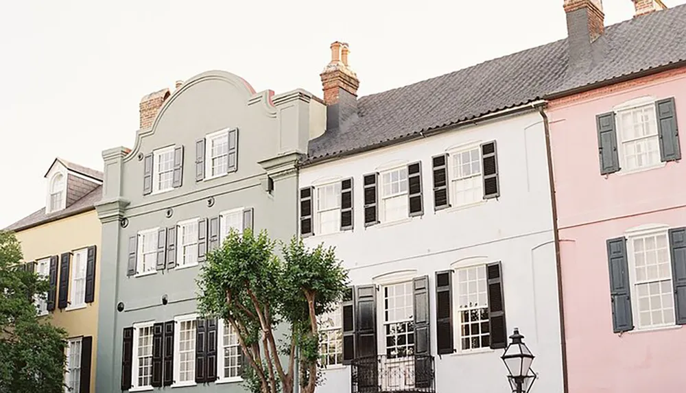 The image shows a row of charming pastel-colored houses with traditional shutters under a soft sky