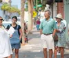 A group of people are attentively listening to a woman gesturing with her hand as if she is guiding a tour on a city street