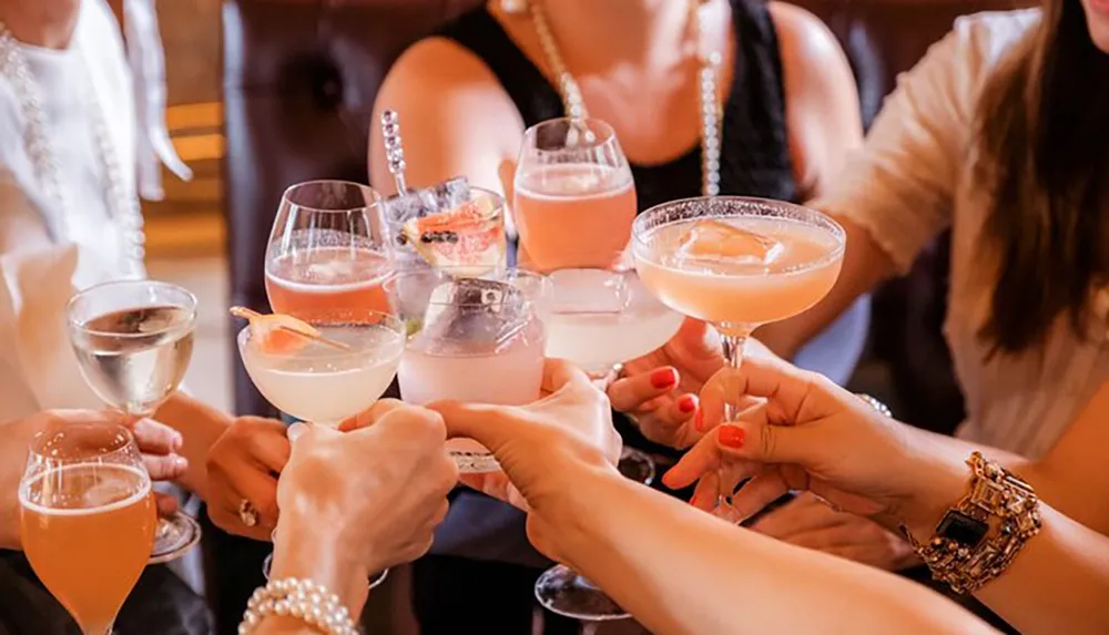 A group of people are cheerfully clinking various cocktail glasses together in a celebratory manner