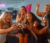 Five women are smiling for a photo at a table with drinks in a social setting