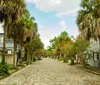 The image shows a classic southern-style manor with large columns surrounded by a lush garden and Spanish moss-draped trees where people are leisurely spending time in its tranquil setting