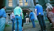 A group of people is listening attentively to a guide who is speaking in front of a historic building with barred windows.