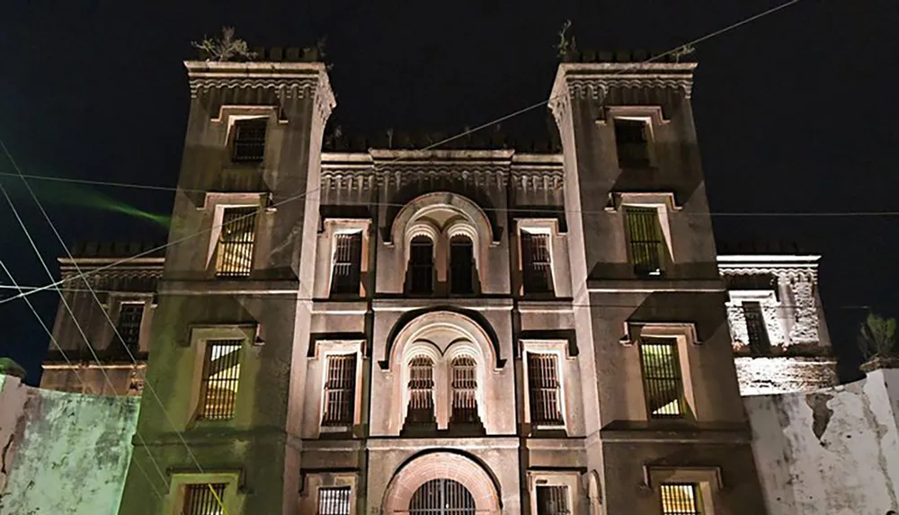 The image shows a symmetrical illuminated facade of a grand building at night with architectural details highlighted against a dark sky