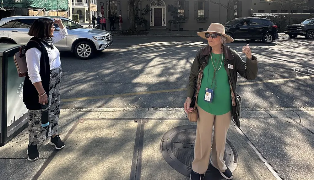 Two individuals are standing on a sidewalk one appears to be guiding or explaining something to the other near a street with cars passing by