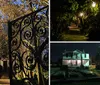 An ornate wrought iron gate stands partly open to a warmly lit garden pathway at twilight