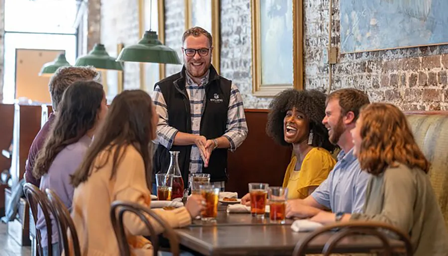 A group of people enjoy a lively conversation with a smiling waiter in a cozy restaurant setting.