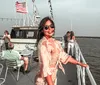 A smiling woman in sunglasses poses on the deck of a boat with other passengers and the American flag fluttering in the background