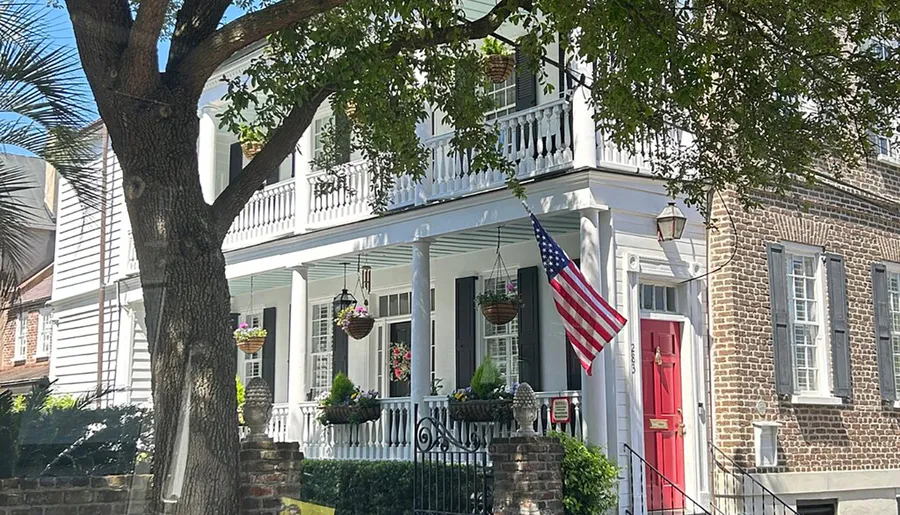 The image shows a charming two-story house with a white facade, a red door, American flag, and hanging flower baskets, evoking a sense of traditional American residential architecture.