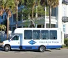 A Gray Line tour shuttle bus is parked on a sunny street in front of an elegant building with palm trees