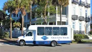 A Gray Line tour shuttle bus is parked on a sunny street in front of an elegant building with palm trees.