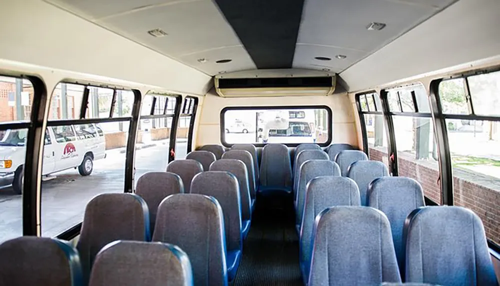 The image shows the interior of an empty shuttle bus with rows of blue and gray seats and large windows