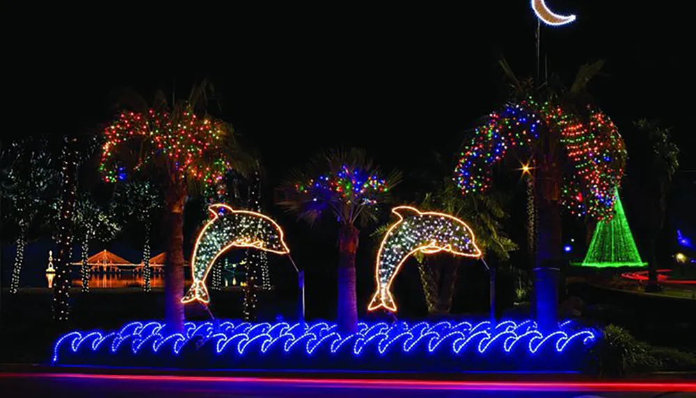 The image features a colorful holiday light display with illuminated dolphins jumping over waves surrounded by palm trees adorned with multicolored lights