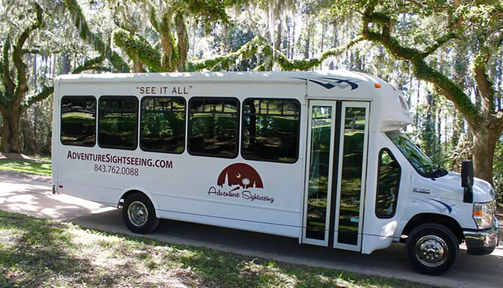 A white sightseeing bus from Adventure Sightseeing is parked on a scenic path surrounded by trees with hanging moss