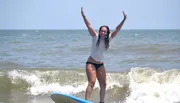 An exuberant person celebrates while successfully surfing a small wave.
