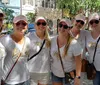 A group of women wearing matching white t-shirts and pink caps with one wearing a shirt labeled Bride and the others Team Bride are smiling together likely at a bachelorette party
