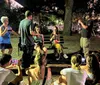 A group of people gather at night in a park some standing and others sitting on benches with attention seemingly focused towards the center under artificial light